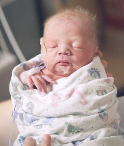 Newborn wrapped in a blanket with a parenteral access on the hand