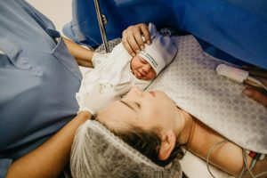 A woman cradles a baby while a nurse supports the baby, highlighting a nurturing environment. It's about Improving Therapeutic Hypothermia for Newborns.